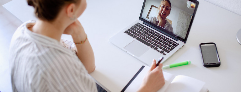 Digitales Lernen Am Schreibtisch sitzende Studentin schaut ein Lernvideo, daneben liegen Bücher und Stifte.