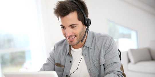 Mann sitzt vor dem Laptop und hat ein Headset auf.